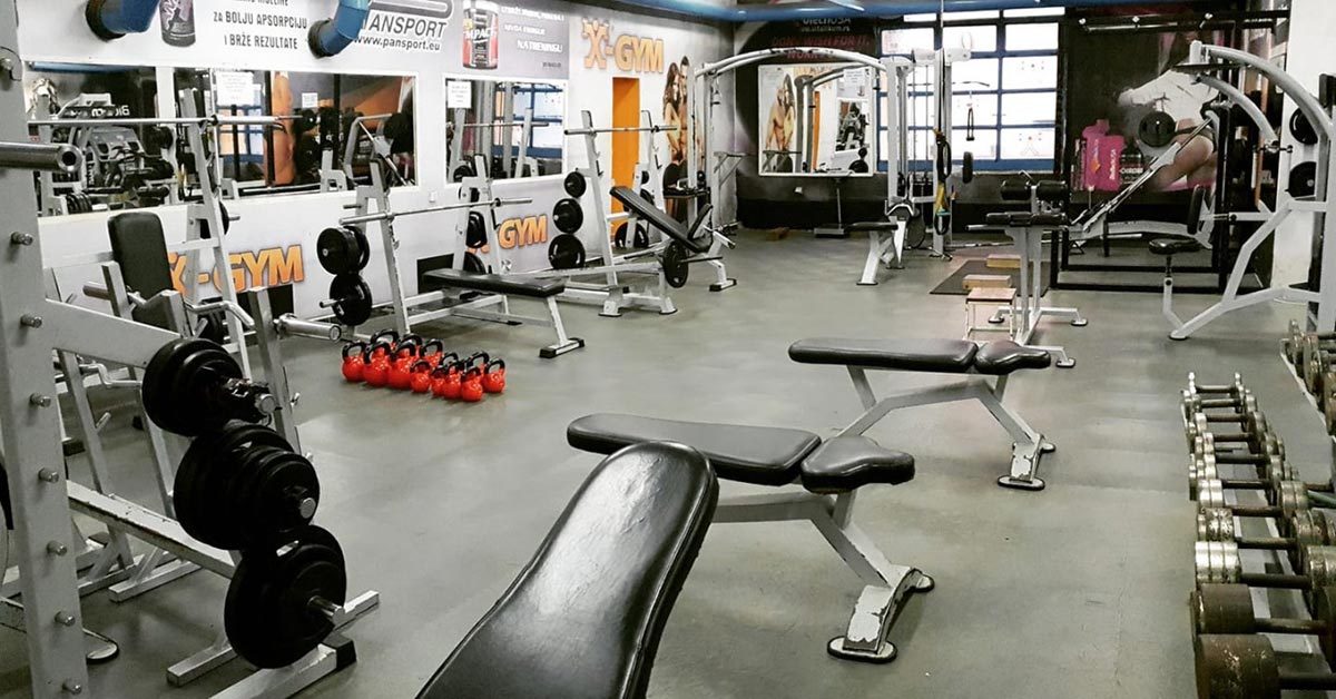 Fitnessstudio mit Hantelbänken und Geräten auf grauem Boden